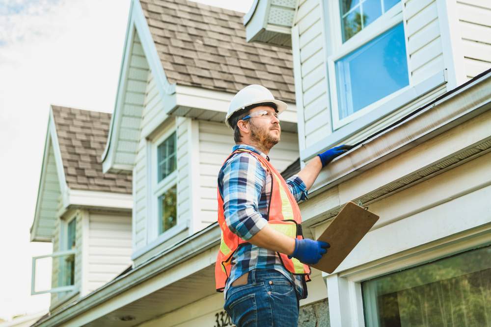 man with hard hat standing on steps inspecting house roof