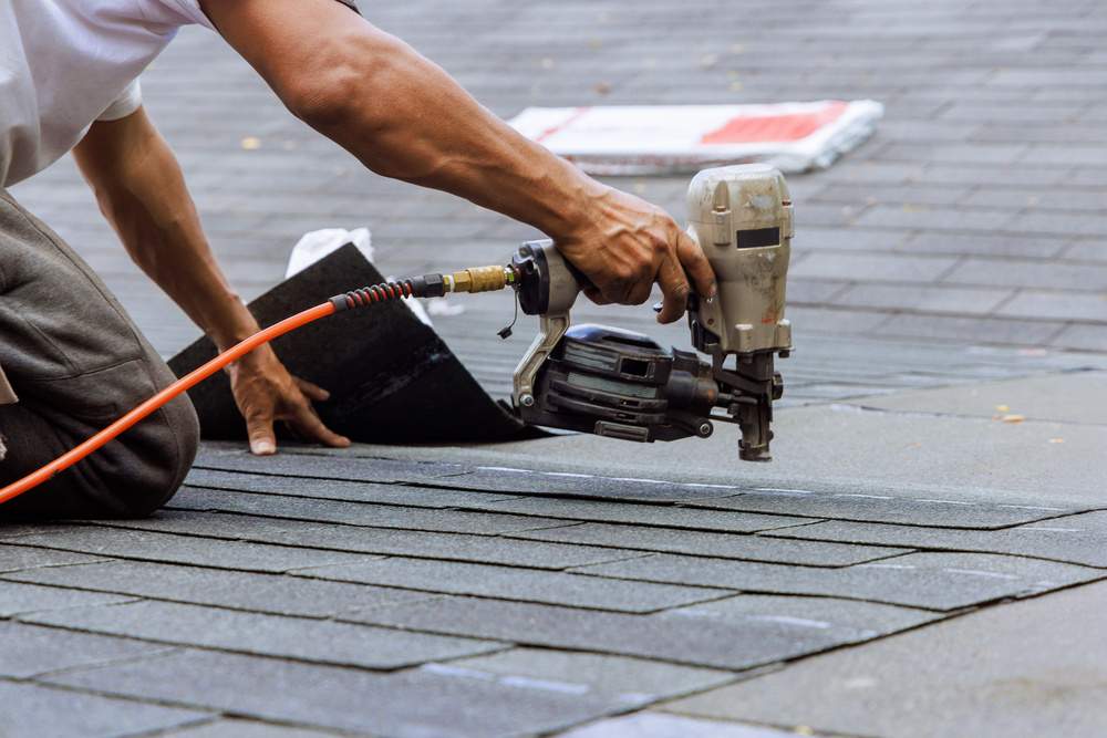 Air pneumatic nail gun used by roofer to install new asphalt bitumen a shingles