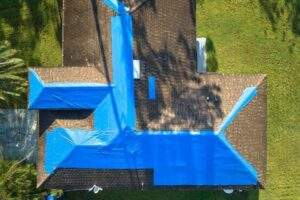 Top view leaking house roof covered with protective tarp sheets against rain water leaks until replacement asphalt shingles damage building rooftop as aftermath