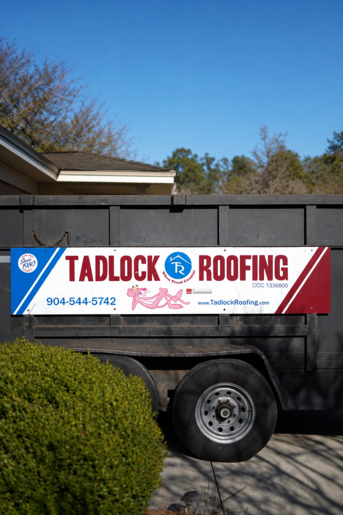 Side of a black dump truck with a Tadlock Roofing advertising banner visible on the side, including the company name and phone number 904-544-5742.